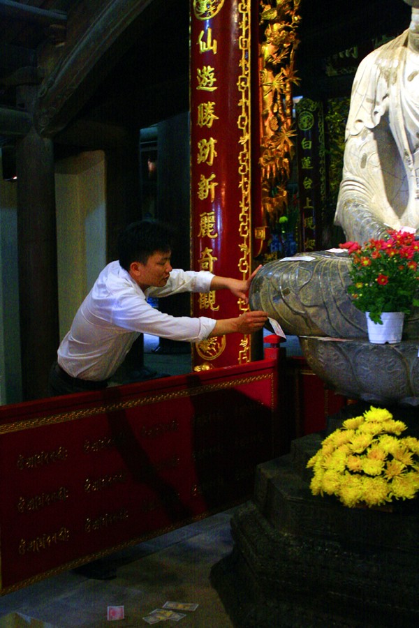 Một du khách tìm cách nhét tiền xuống dưới bệ của tượng Phật